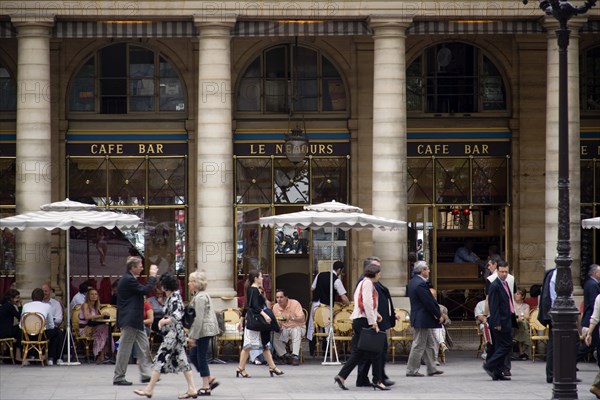 FRANCE, Ile de France, Paris, People at tables with pedestrians walking past outside the Cafe Bar Le Nemours in Place Colette