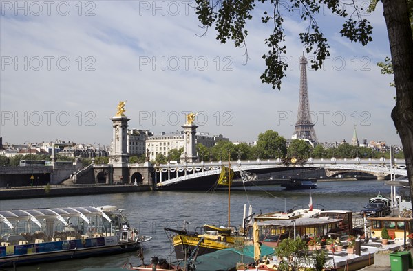 FRANCE, Ile de France, Paris, Houseboat barges moored at the Port des Champs Elysees on the River Seine with the Pont Alexandre III bridge and the Eiffel Tower beyond