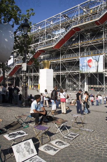 FRANCE, Ile de France, Paris, Tourists watching a street performer in the square outside the Pompidou Centre in Beauborg Les Halles with artists selling their work on the pavement in the foreground
