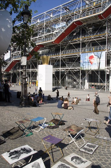 FRANCE, Ile de France, Paris, Tourists watching a street performer in the square outside the Pompidou Centre in Beauborg Les Halles with artists selling their work on the pavement in the foreground