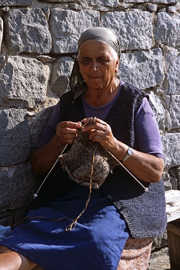 BULGARIA, Bansko, Old lady sitting on bench knitting.