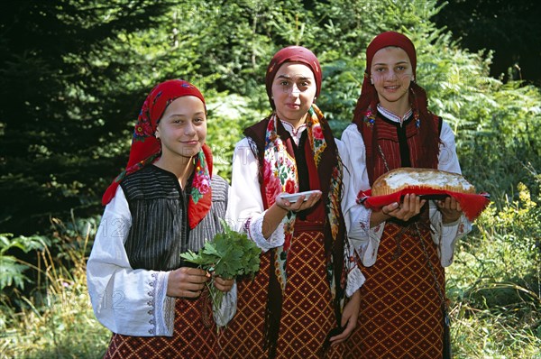 BULGARIA, Pirin Mountain, Chalin Valog, "Girls dressed in Bulgarian national costume holding bread, salt and leaves."