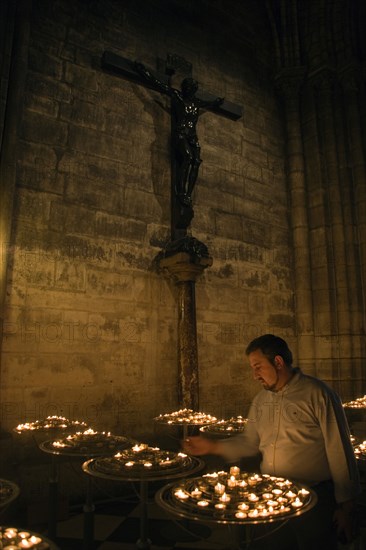 FRANCE, Ile de France, Paris, Man lighting votive candles below a cross with Christ crucified in a chapel within the Gothic Cathedral of Notre Dame on the Ile de la Cite
