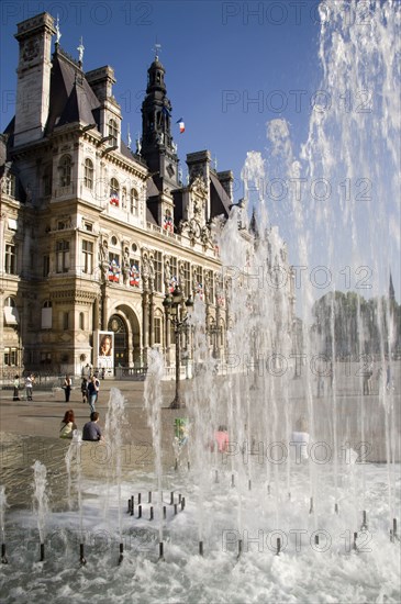 FRANCE, Ile de France, Paris, The Hotel de Ville town hall with people in the square in front of it seen through a water fountain