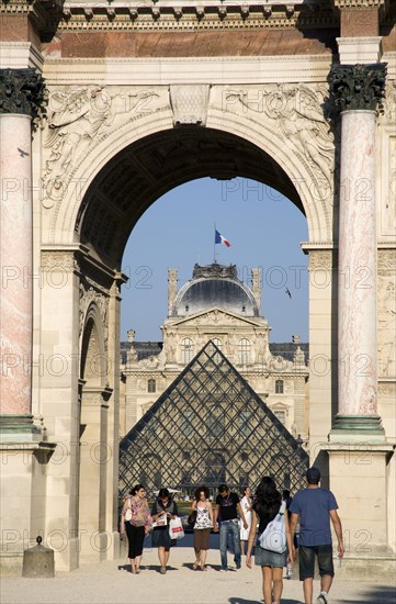 FRANCE, Ile de France, Paris, People walking from the Jardin des Tuileries through the Arc de Triomphe du Carrousel towards the pyramid entrance to the Musee du Louvre