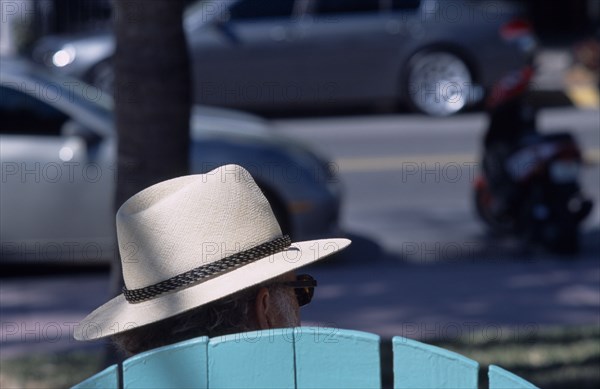 USA, Florida, Miami, South Beach. Ocean Drive. The head of a man wearing a Panama hat seen above the top of a seat watching people and traffic go by
