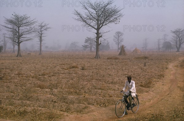 NIGERIA, Environment, "Dry and dusty northeast tradewind or harmattan blowing over groundnut fields near Kaduna, an area of arid agricultural land.  Cyclist in foreground."
