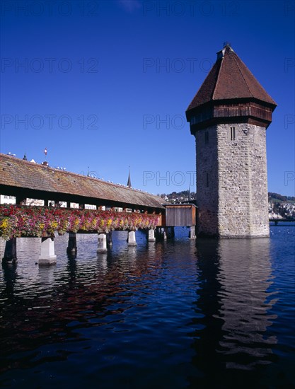 SWITZERLAND, Lucerne Central, Lucerne, Kappelbrucke flower decked covered bridge spanning across The River Reuss. Part  view with Wasserturm 13th Century octagonal Tower