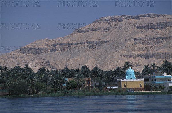 EGYPT, Nile Valley, Luxor, View across the River Nile towards a Mosque on the West Bank with a turquoise domed roof amongst dense palm trees