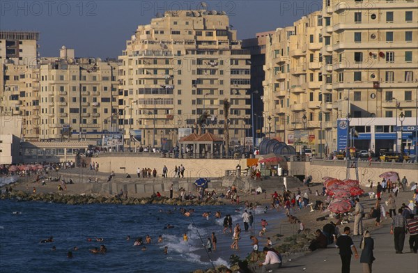 EGYPT, Nile Delta, Alexandria, "Corniche Waterfront seen in golden light. Busy beach with people swimming in the sea, fishing from the waters edge and walking on the promenade. Overlooked by tall buildings."