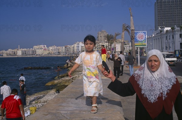EGYPT, Nile Delta, Alexandria, Corniche Waterfront. A mother wearing an Islamic headscarf holding her daughters hand while she walks along wall above her.
