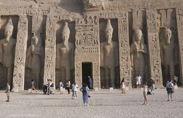EGYPT, Nile Valley, Abu Simbel, Hathor Temple . Built for Ramses II's wife Nefertari. Six standing statues caved into facade. Visitors walking in the grounds.