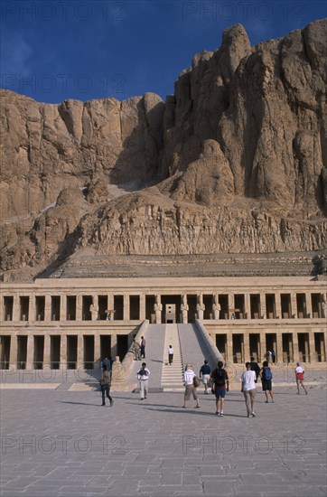 EGYPT, Nile Valley, Thebes, Deir el-Bahri. Hatshepsut Mortuary Temple. Visitors walking towards ramped entrance with limestone cliffs behind.