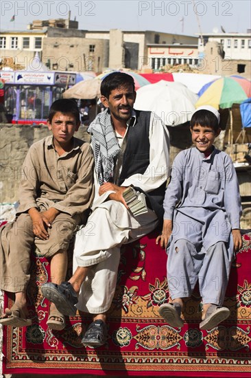 AFGHANISTAN, Kabul, Money changer sits on rug on walls of Kabul river with street boys