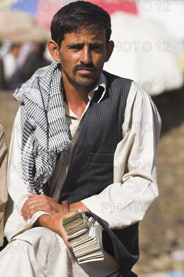 AFGHANISTAN, Kabul, Money changer sits on rug on walls of Kabul river