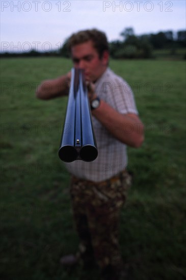 20085232 SPORT Shooting Guns Man holding double barrelled shotgun with detail of the tip of the gun in focus.