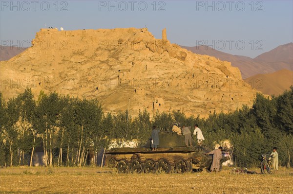 AFGHANISTAN, Bamiyan Province, Bamiyan, "Children playing on abandoned tanks in fied in front of Ruined citadel of Shahr-e-Gholgola known as City of the Screaming