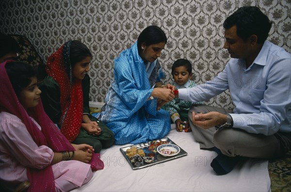 ENGLAND, Religion, Hindu, Woman tying thread on wrist of man during the Sacred Thread ceremony. The Hindu male rite of passage ceremony