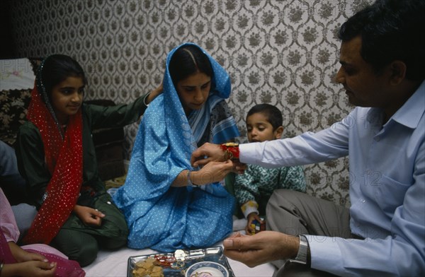 ENGLAND, Religion, Hindu, Woman tying thread on wrist of man during the Sacred Thread ceremony. The Hindu male rite of passage ceremony