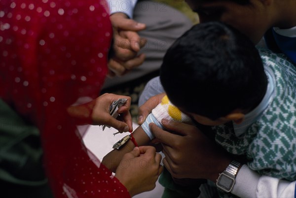 ENGLAND, Religion, Woman tying thread on arm of boy during the Sacred Thread ceremony. The Hindu male rite of passage ceremony