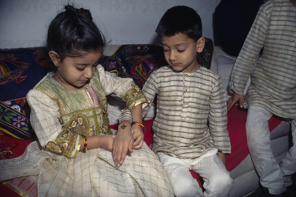 ENGLAND, Religion, Hindu, Young girl tying a thread to the wrist of a young boy during the Sacred Thread ceremony. The Hindu male rite of passage ceremony