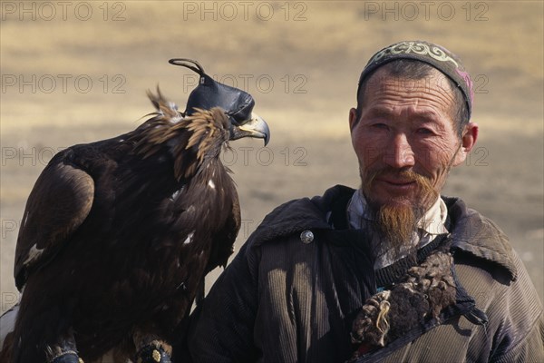 MONGOLIA, People, Head and shoulders portrait of Kazakh nomad man with golden eagle wearing hood and jesses.