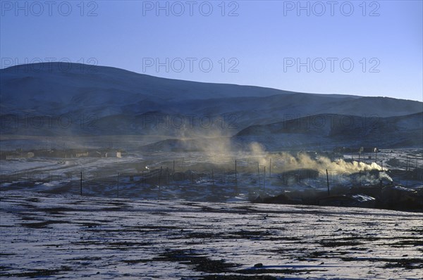MONGOLIA, Hovd Province, Erdeneburen, Drifting smoke from buildings in landscape with light covering of snow in March sunset.
