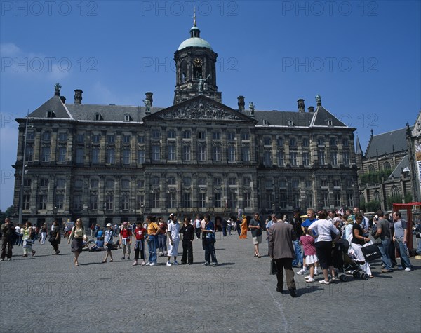 HOLLAND, Noord-Holland, Amsterdam, "Damm Square.  Royal Palace exterior facade with domed clock tower and weather vane, pediment with relief carving and multiple windows.  Crowds in foreground."