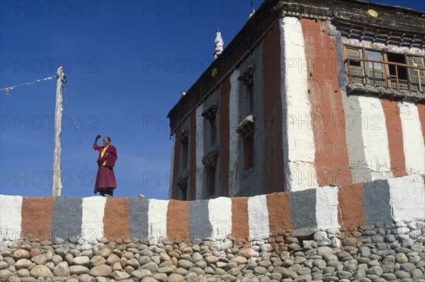 NEPAL, Mustang, Tsarang Gompa, "Tibetan Buddhist monk looking out from monastery terrace, shielding his eyes from the sun."