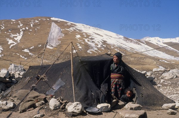 NEPAL, Mustang, Nomads, "Tibetan nomad encampment on the high plateau, woman and child looking out from entrance of tent with light covering of snow on mountainside behind."