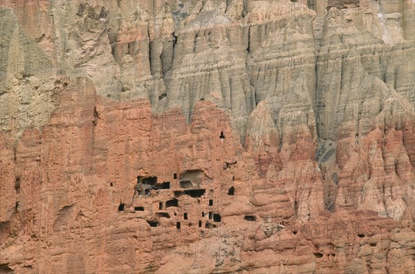 NEPAL, Mustang, Drakhmar, "Ancient cave dwellings in steep, eroded grey and orange coloured cliff face."