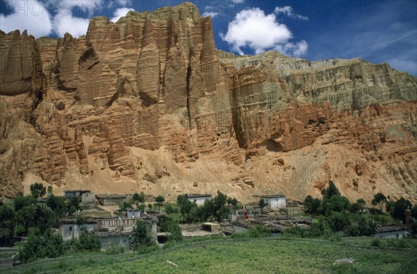 NEPAL, Mustang, Drakhmar, "Summer landscape.  Adobe village housing and cultivated land at foot of steep, eroded cliff.  "