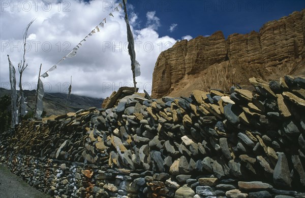 NEPAL, Mustang, Drakhmar, Prayer wall made from stacked stones engraved with prayers and with prayer flags flying above.