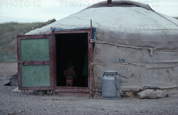 MONGOLIA, Architecture, Young child standing inside open doorway of yurt wearing just a jumper and no trousers.