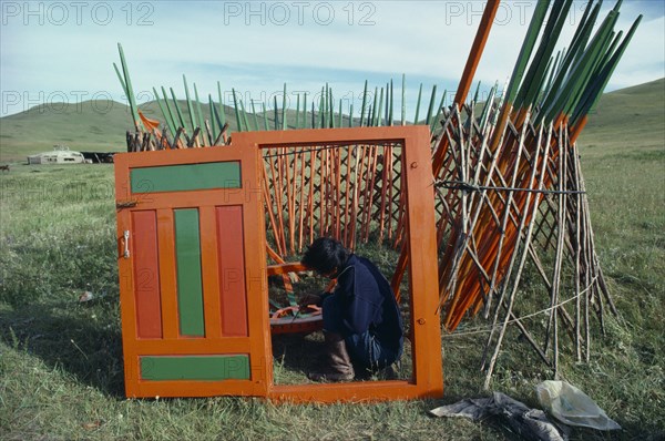 MONGOLIA, Architecture, Man painting interior framework of yurt sitting within circular lattice structure framed by newly painted open doorway.