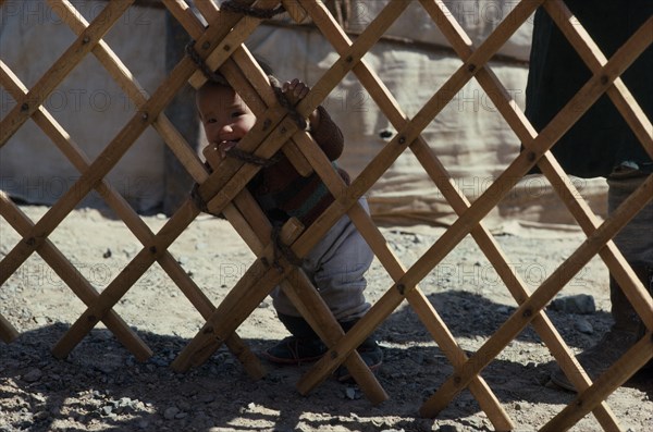 MONGOLIA, South Gobi, Children, Toddler looking out through lattice framework of yurt.