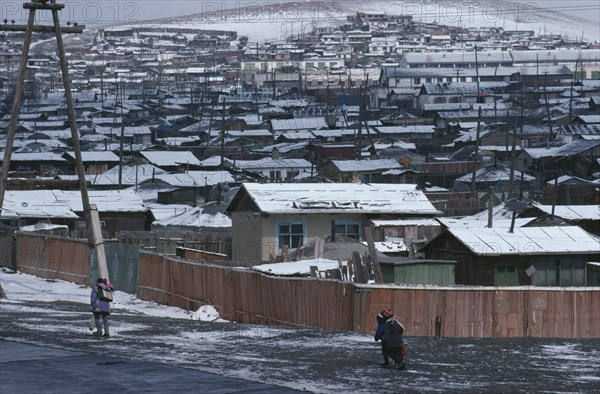 MONGOLIA, Ulan Bator, Snow covered rooftops of housing in city suburbs in winter with children wrapped up in warm clothing walking along road in foreground.