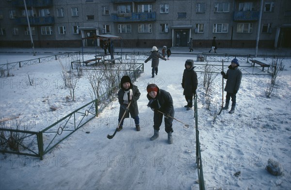 MONGOLIA, Ulan Bator, Children playing ice hockey along pavements in winter snow.