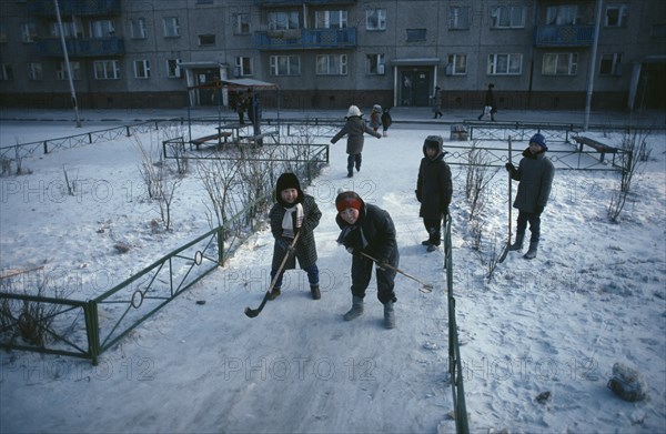 MONGOLIA, Ulan Bator, Children playing ice hockey along pavements in winter snow.