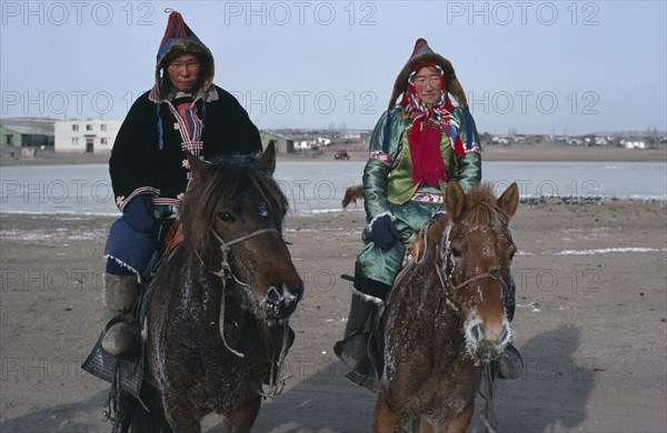 MONGOLIA, People, Buriyat ethnic minority couple in traditional dress riding horses with frosted coats and whiskers.