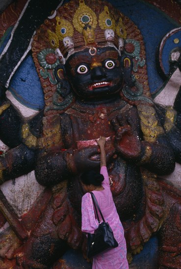 NEPAL, Kathmandu, Woman making offerings at the Kala Bhairab or black Shiva in Durbar Square representing the fearsome Tantric form of Shiva in Nepal.