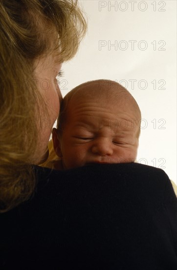 ENGLAND, Gestures, Mother holding face against three week old son carried on her shoulder.