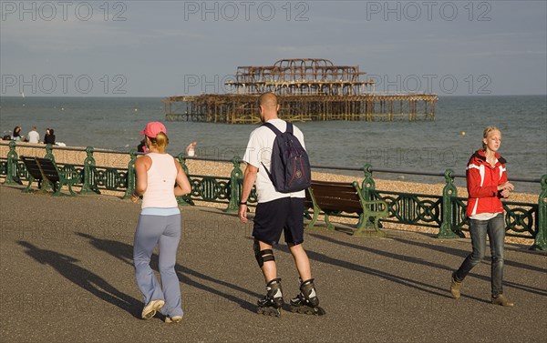ENGLAND, East Sussex, Brighton, Woman jogging with man rollerblading on the seafront promenade.