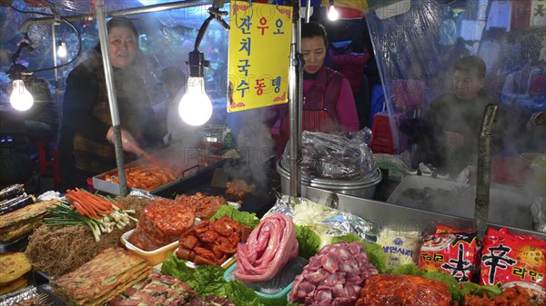 KOREA, South, Seoul, "Namdaemun - Namdaemun market, December evening, food stall, women cooking, customers eating, stacks of meat and fish waiting to be cooked"