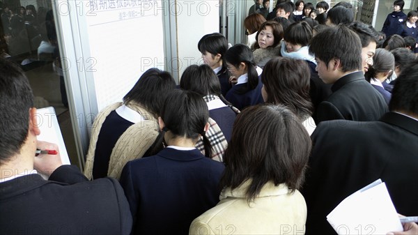 JAPAN, Honshu, Tokyo, "Chiba, Sosa - Yokaichiba Kei Ai High School, 14 and 15 year old third year junior high school students crowd to see if their number is posted meaning they passed the high school entrance exam"