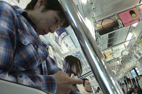 JAPAN, Honshu, Tokyo, "JR train, a young man uses his cell phone, text message"