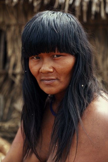 BRAZIL, Mato Grosso, Indigenous Park of the Xingu, Head and shoulders portrait of young  Panara woman outside thatched home part seen behind. Formally known as Kreen-Akrore  Krenhakarore  Krenakore  Krenakarore  Amazon American Brasil Brazilian Female Women Girl Lady Indegent Kreen Akore Latin America Latino South America Female Woman Girl Lady Immature One individual Solo Lone Solitary