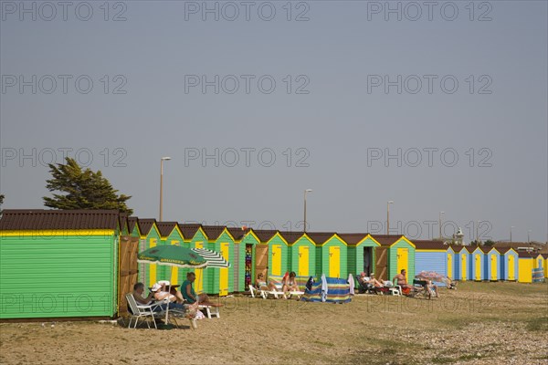 ENGLAND, West Sussex, Littlehampton, Green and yellow beach huts on shingle beach with sunbathers on sun loungers