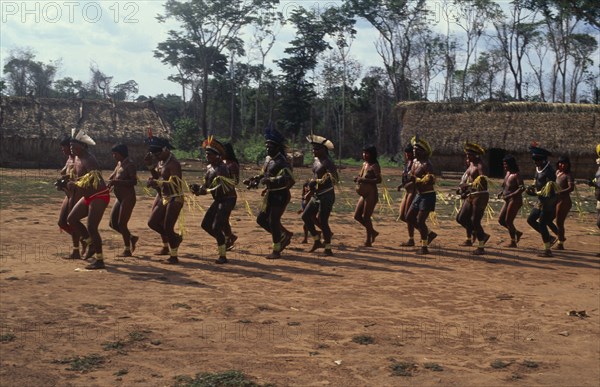 BRAZIL, Mato Grosso, Indigenous Park of the Xingu, Panar‡ men and women performing traditional dance around central area of village.  Men wearing head-dresses or crowns of feathers and face and body paint. Formally known as Kreen-Akrore  Krenhakarore  Krenakore  Krenakarore  Amazon American Brasil Brazilian Classic Classical Female Woman Girl Lady Historical Indegent Kreen Akore Latin America Latino Male Man Guy Older Performance South America
