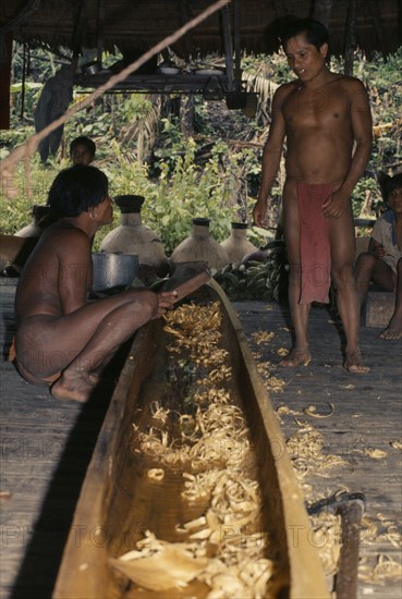 COLOMBIA, Choco, Embera Indigenous People, Two Embera men discuss final shaping of wooden dug-out canoe on floor of thatched shelter beside their riverside home. Pacific coastal region boat canoa tribe American Colombian Colombia Hispanic Indegent Latin America Latino Male Men Guy South America  Pacific coastal region boat piragua tribe American Colombian Columbia Hispanic Indegent Latin America Latino Male Men Guy South America Male Man Guy 2